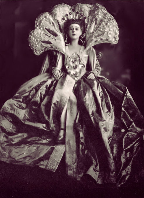Photograph, Marie Gutheil-Schoder as Potiphar's Wife, Marie Gutheil-Schoder als Frau Potiphar, by Franz Xaver Setzer, 1922. Theatermuseum, Vienna / Photoatelier Setzer-Tschiedel. Black and white studio photograph of a woman standing in a wide, voluminous stage gown with a heavily structured bodice featuring metallic ornaments. She wears a high, ornate fan-shaped collar encrusted with rows of pearls or beads, a crown on her dark hair, and looks directly forward against a dark vignette backdrop.