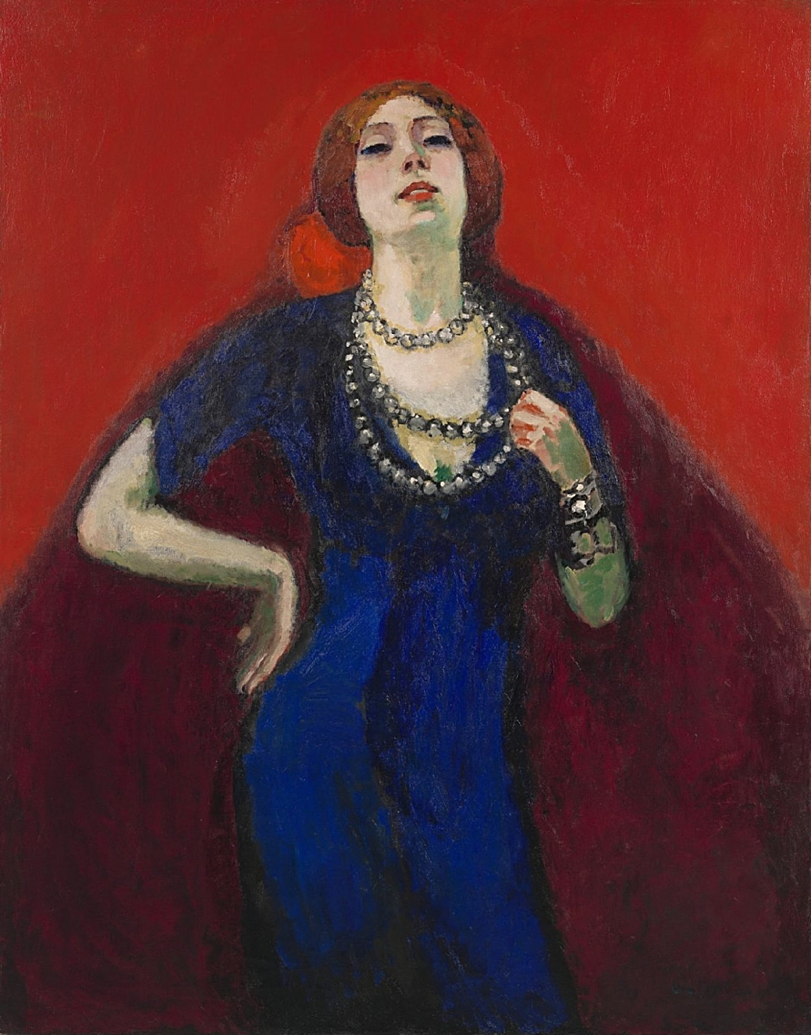 Oil on canvas, The Blue Dress, La robe bleue, by Kees van Dongen, 1911. Van Gogh Museum. A front-facing portrait of a woman with her right hand resting on her hip and her left hand touching a long pearl necklace against a solid crimson backdrop.